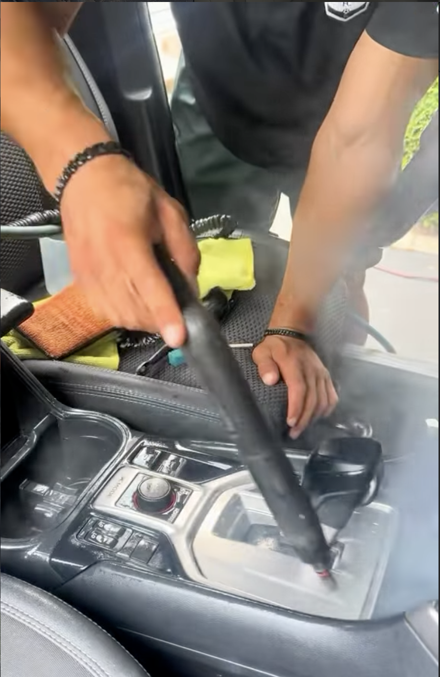 Technician steam cleaning a center console and shifter during an on-site interior detail