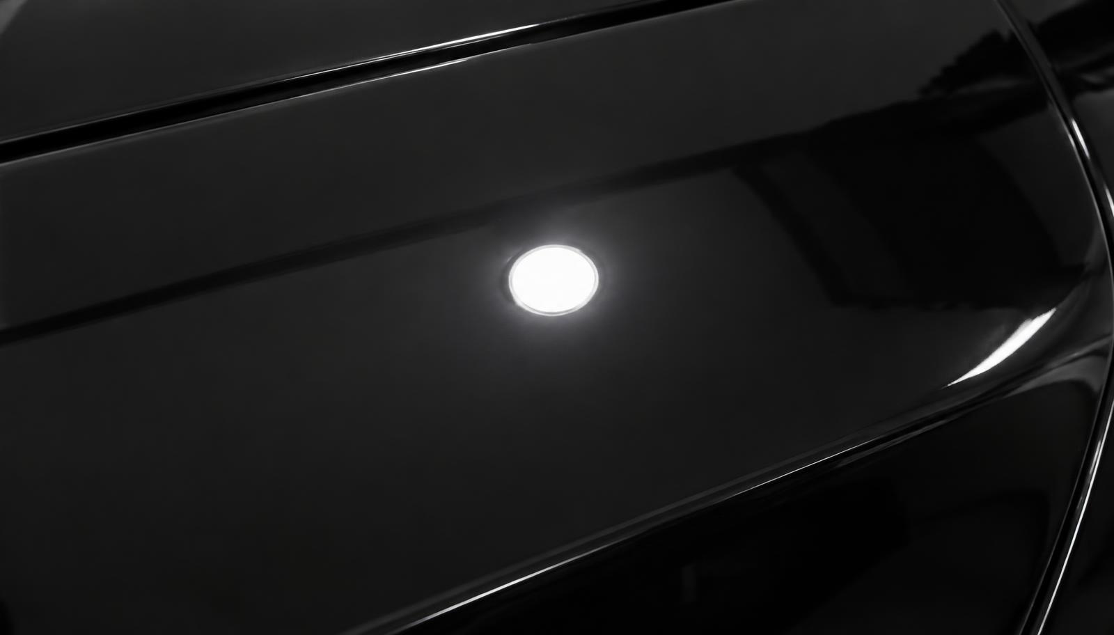 The same dark car panel after three-stage paint correction, defect free under inspection light